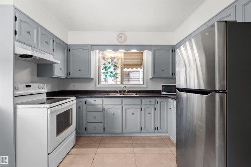 Kitchen featuring light gray cabinetry, dark countertops, a stainless steel refrigerator, white electric range, and tile flooring - 8723 81 Avenue Nw, Edmonton, AB - Indoor Photo Showing Kitchen With Double Sink