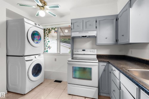 Stacked laundry appliances, white electric range, wood-finish cabinetry, dark speckled countertop, and tiled flooring - 8723 81 Avenue Nw, Edmonton, AB - Indoor Photo Showing Laundry Room