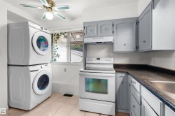 Stacked laundry appliances, white electric range, wood-finish cabinetry, dark speckled countertop, and tiled flooring - 