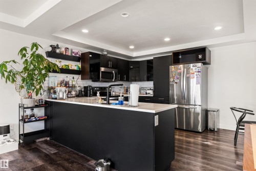 Kitchen featuring dark wood-finish flooring, recessed lighting, white tray ceiling, dark cabinetry, and a large central island with a white countertop - 15713 102 Avenue Nw, Edmonton, AB - Indoor Photo Showing Kitchen With Upgraded Kitchen