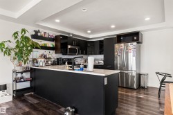 Kitchen featuring dark wood-finish flooring, recessed lighting, white tray ceiling, dark cabinetry, and a large central island with a white countertop - 