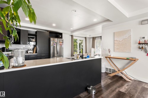 Kitchen featuring a large island with a light-toned countertop, dark cabinetry, stainless steel appliances, and wood-finish flooring - 15713 102 Avenue Nw, Edmonton, AB - Indoor Photo Showing Other Room