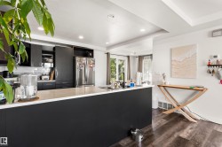 Kitchen featuring a large island with a light-toned countertop, dark cabinetry, stainless steel appliances, and wood-finish flooring - 