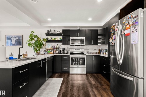 Modern kitchen featuring dark cabinetry, stainless steel appliances, light countertops, a tile backsplash, and wood-finish flooring - 15713 102 Avenue Nw, Edmonton, AB - Indoor Photo Showing Kitchen With Stainless Steel Kitchen With Double Sink With Upgraded Kitchen