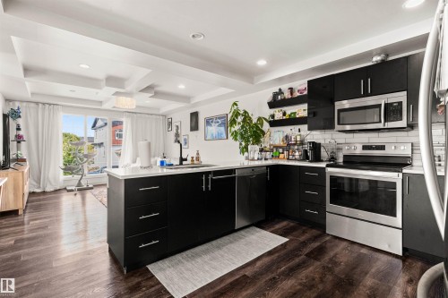 Modern kitchen featuring dark cabinetry, stainless steel appliances, a white subway tile backsplash, and an island with a white countertop - 15713 102 Avenue Nw, Edmonton, AB - Indoor Photo Showing Kitchen With Upgraded Kitchen