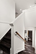 Dark wood-finish flooring with white trim, a wood handrail, and recessed lighting - 