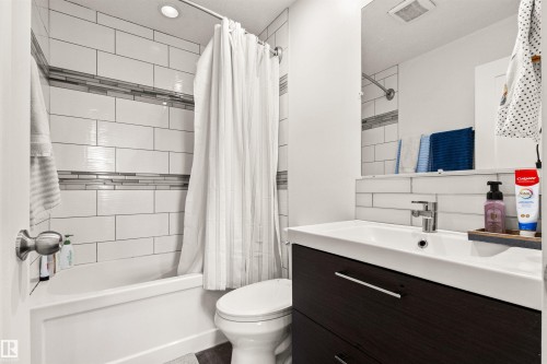 Bathroom featuring a bathtub with subway tile surround, decorative tile accent band, built-in vanity with under-sink storage, and a single-handle faucet - 15713 102 Avenue Nw, Edmonton, AB - Indoor Photo Showing Bathroom