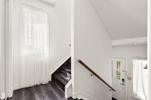 Dark wood-finish flooring with a matching staircase, white walls, and a window with sheer white drapery - 15713 102 Avenue Nw, Edmonton, AB - Indoor Photo Showing Other Room