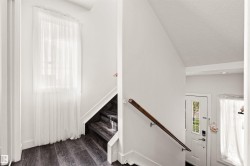 Dark wood-finish flooring with a matching staircase, white walls, and a window with sheer white drapery - 