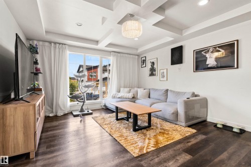 Expansive window offering abundant natural light, tray ceiling with recessed lighting, wood-finish flooring throughout, and a contemporary chandelier fixture - 15713 102 Avenue Nw, Edmonton, AB - Indoor Photo Showing Living Room
