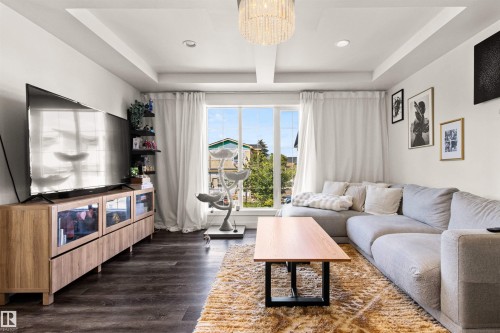 Wood-finish flooring, recessed lighting, tray ceiling, large windows with white drapes, and a contemporary chandelier - 15713 102 Avenue Nw, Edmonton, AB - Indoor Photo Showing Living Room