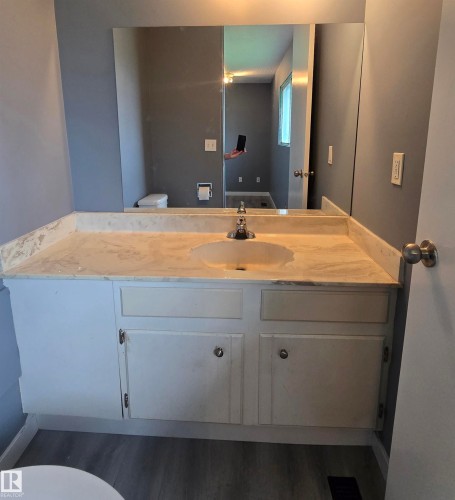 Vanity with an integrated sink and a marbled-finish countertop, featuring a full-width wall mirror and under-sink cabinetry - 10829 167A Avenue Nw, Edmonton, AB - Indoor Photo Showing Bathroom