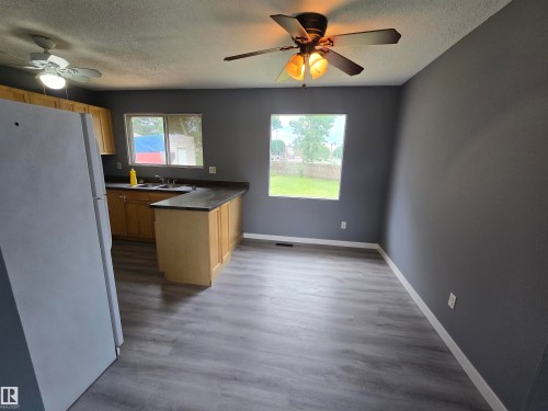 Wood-finish flooring, light wood cabinetry, dark countertops, and ceiling fans - 10829 167A Avenue Nw, Edmonton, AB - Indoor Photo Showing Other Room