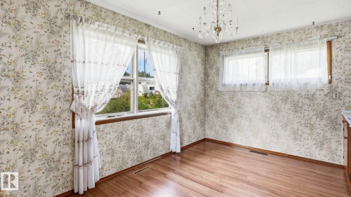 Wood-finish flooring with floral pattern wallpaper, a crystal chandelier, and multiple windows - 52012 Hwy 21, Rural Strathcona County, AB - Indoor Photo Showing Other Room