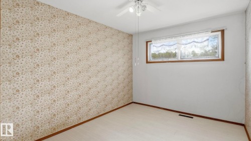Patterned wallpaper accent wall, wood-finish flooring, and a ceiling fan with integrated lighting - 52012 Hwy 21, Rural Strathcona County, AB - Indoor Photo Showing Other Room