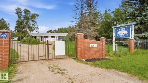 Gated entry with brick pillars, a long driveway, and a white single-story structure with a dark roof - 52012 Hwy 21, Rural Strathcona County, AB - Outdoor
