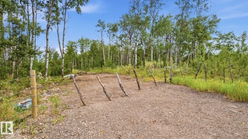 Gravel area with a partial barbed wire fence and natural wood posts, bordered by varied foliage and mature trees - 52012 Hwy 21, Rural Strathcona County, AB - Outdoor