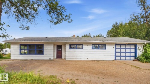 Ranch-style residence featuring white siding, a dark roof, blue window frames, and an integrated garage with a blue sectional door - 52012 Hwy 21, Rural Strathcona County, AB - Outdoor
