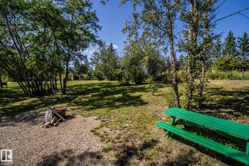 Expansive outdoor space featuring a graveled fire pit area, a green picnic table, and mature deciduous trees - 347, 58532 Range Rd 113, Rural St. Paul County, AB 