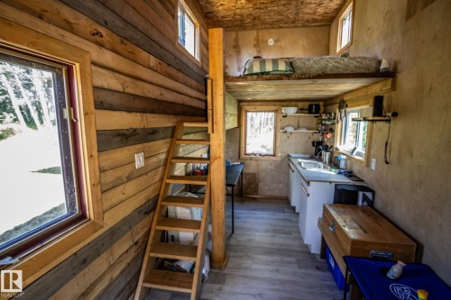Wood-paneled interior walls, natural light from multiple windows, built-in wooden staircase, compact kitchen with white cabinetry and sink, and a lofted sleeping area - 347, 58532 Range Rd 113, Rural St. Paul County, AB 