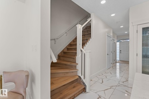 Hardwood staircase with wrought iron balusters, white trim, recessed lighting, and white marble-look tile flooring - 5415 167A Avenue Nw, Edmonton, AB - Indoor Photo Showing Other Room