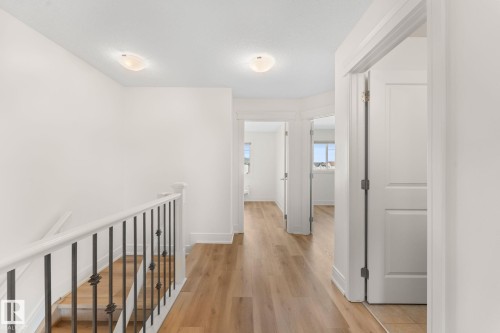 Wood-finish flooring throughout the hallway, white interior doors, and a staircase featuring a white handrail with black iron balusters - 5415 167A Avenue Nw, Edmonton, AB - Indoor Photo Showing Other Room