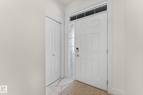Entryway featuring white six-panel door with decorative glass sidelight and transom, bi-fold closet doors, and patterned tile flooring - 5415 167A Avenue Nw, Edmonton, AB - Indoor Photo Showing Other Room