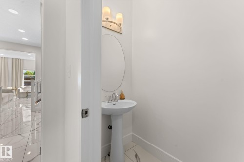 Pedestal sink with chrome faucet, oval wall mirror, and modern wall sconce lighting - 5415 167A Avenue Nw, Edmonton, AB - Indoor Photo Showing Bathroom