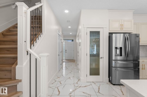 Hardwood staircase with wrought iron balusters, stainless steel refrigerator, white cabinetry with gold-toned hardware, white solid surface countertop, and large format floor tiling - 5415 167A Avenue Nw, Edmonton, AB - Indoor Photo Showing Other Room