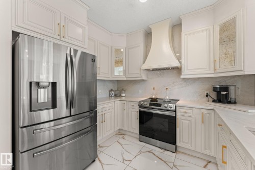 Stainless steel refrigerator, built-in range, custom cabinetry, decorative range hood, and stone countertops - 5415 167A Avenue Nw, Edmonton, AB - Indoor Photo Showing Kitchen