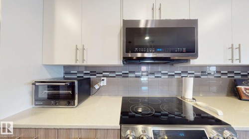 White upper cabinetry, stainless steel microwave, glass cooktop, light-toned countertops, and a decorative tile backsplash - 17359 49 Street Nw, Edmonton, AB - Indoor Photo Showing Kitchen