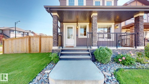 Covered front porch with stone-clad columns, dark wood-finish siding, white framed windows, and a concrete walkway - 17359 49 Street Nw, Edmonton, AB - Outdoor