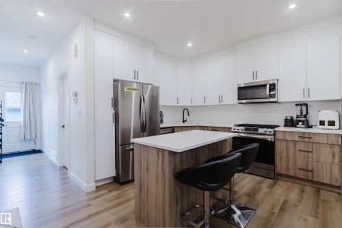 Contemporary kitchen with two-tone cabinetry, stainless steel appliances, a center island with countertop seating, and wood-finish flooring - 104 Meadowview Way, Leduc, AB - Indoor Photo Showing Kitchen With Upgraded Kitchen
