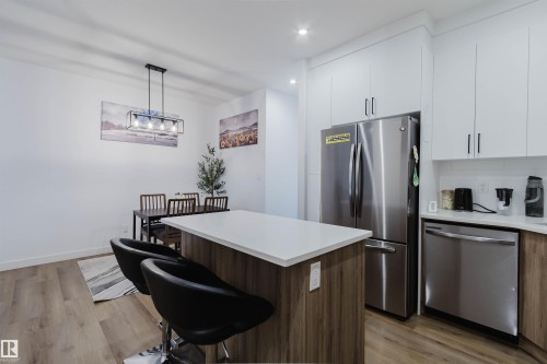 Kitchen featuring a wood-finish island with a light-toned countertop, stainless steel appliances, white upper cabinetry, and wood-finish lower cabinetry - 104 Meadowview Way, Leduc, AB - Indoor Photo Showing Kitchen