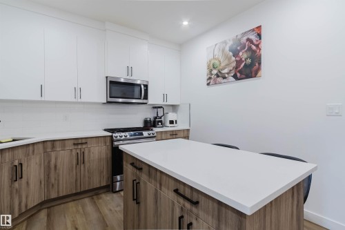 Kitchen featuring wood-finish flooring, two-tone cabinetry with matte black hardware, stainless steel appliances, a white subway tile backsplash, and white countertops - 104 Meadowview Way, Leduc, AB - Indoor Photo Showing Kitchen