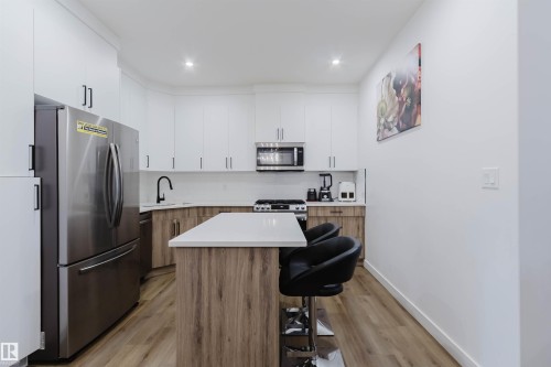 Modern kitchen featuring white upper cabinetry and wood-finish lower cabinetry, white countertops, and wood-finish flooring - 104 Meadowview Way, Leduc, AB - Indoor Photo Showing Kitchen With Upgraded Kitchen