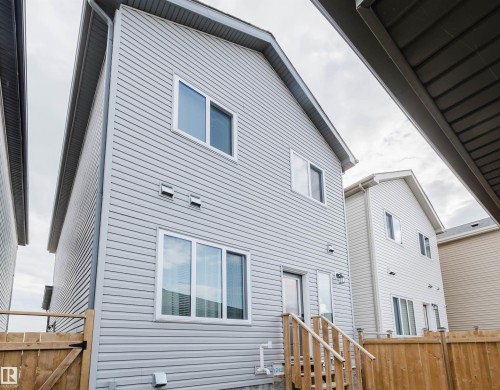Light-toned siding exterior with multiple windows, a rear door, and wood stairs leading to a fenced yard - 104 Meadowview Way, Leduc, AB - Outdoor With Exterior