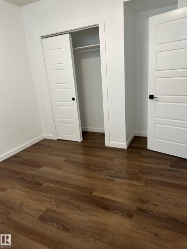 Wood-finish flooring, white paneled doors, sliding closet door with hanging rod, and white trim - 104 Meadowview Way, Leduc, AB - Indoor Photo Showing Other Room