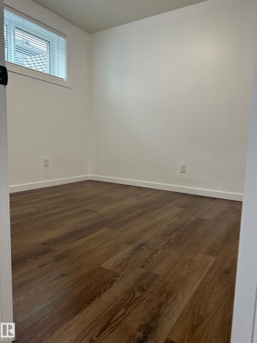 Wood-finish flooring with white baseboards and a horizontal window featuring blinds - 104 Meadowview Way, Leduc, AB - Indoor Photo Showing Other Room