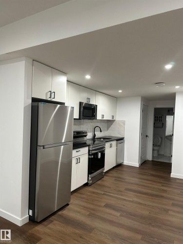 Kitchen featuring white cabinetry, stainless steel appliances, dark countertops, and wood-finish flooring - 104 Meadowview Way, Leduc, AB - Indoor Photo Showing Kitchen