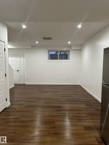 Spacious room with wood-finish flooring, recessed ceiling lighting, and a white paneled door - 104 Meadowview Way, Leduc, AB - Indoor