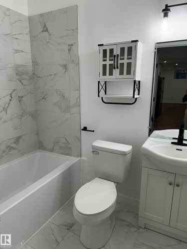 Bathroom featuring a white bathtub, wall-mounted cabinet with glass-front doors, white vanity with an integrated sink, and large format floor and wall tile - 104 Meadowview Way, Leduc, AB - Indoor Photo Showing Bathroom