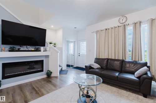 Living area featuring wood-finish flooring, a built-in electric fireplace, recessed lighting, and a white paneled door - 104 Meadowview Way, Leduc, AB - Indoor Photo Showing Living Room With Fireplace