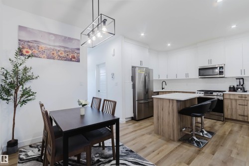 Contemporary kitchen featuring stainless steel appliances, a center island with countertop seating, white upper cabinetry, and wood-finish lower cabinetry - 104 Meadowview Way, Leduc, AB - Indoor