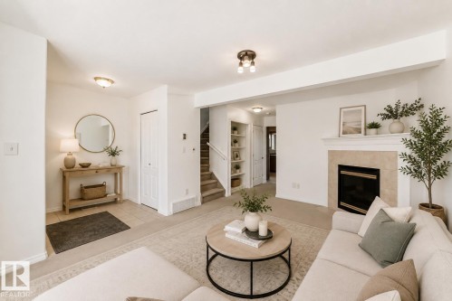Virtually staged room with illustrating potential of room with furniture, decor and new flooring show a recessed fireplace with hearth, built-in shelving, carpeted staircase, and tiled entry - 11727 83 Street Nw, Edmonton, AB - Indoor Photo Showing Living Room With Fireplace