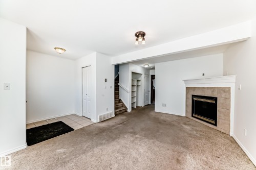 Living area with a tiled fireplace, mantel, built-in shelving, and carpeting - 11727 83 Street Nw, Edmonton, AB - Indoor With Fireplace