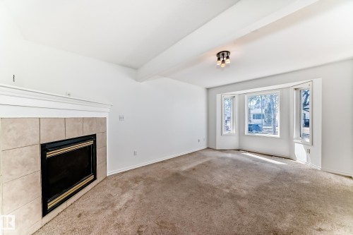 Tile-surround fireplace with mantel, bay window, carpeted flooring, and a flush-mount ceiling light fixture - 11727 83 Street Nw, Edmonton, AB - Indoor With Fireplace