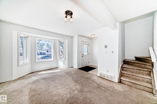 Bay window with multiple panels, front entry door with decorative glass, ceiling-mounted light fixture, and staircase with carpeted treads - 11727 83 Street Nw, Edmonton, AB - Indoor Photo Showing Other Room