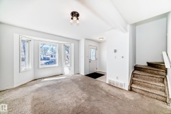 Bay window with multiple panels, front entry door with decorative glass, ceiling-mounted light fixture, and staircase with carpeted treads - 
