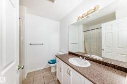 Vanity with a brown speckled countertop and an integrated sink, white cabinetry with gold-tone hardware, a full-width mirror, and a wall-mounted light fixture - 